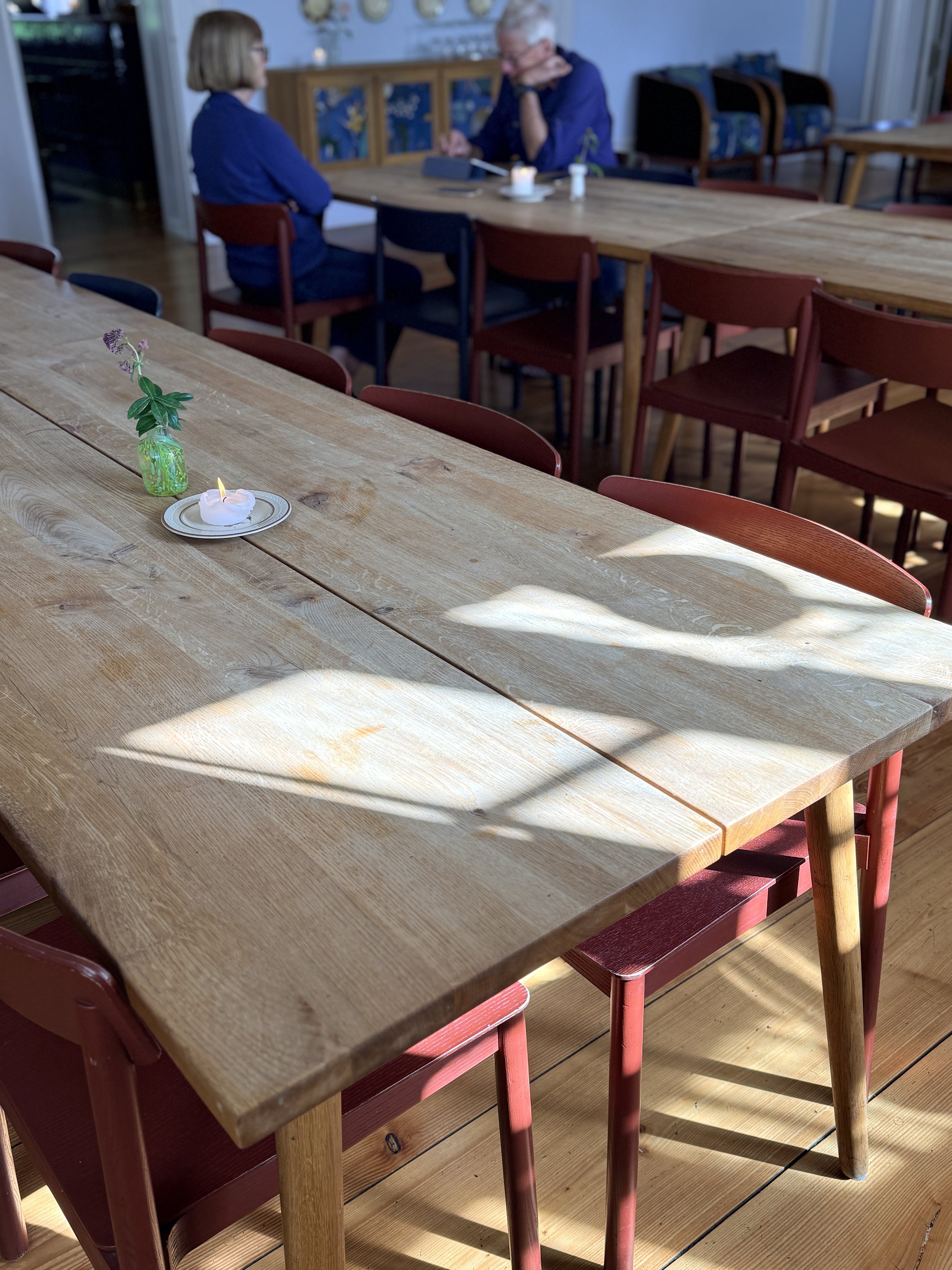 Long timber communal dining table with brick red timber chairs