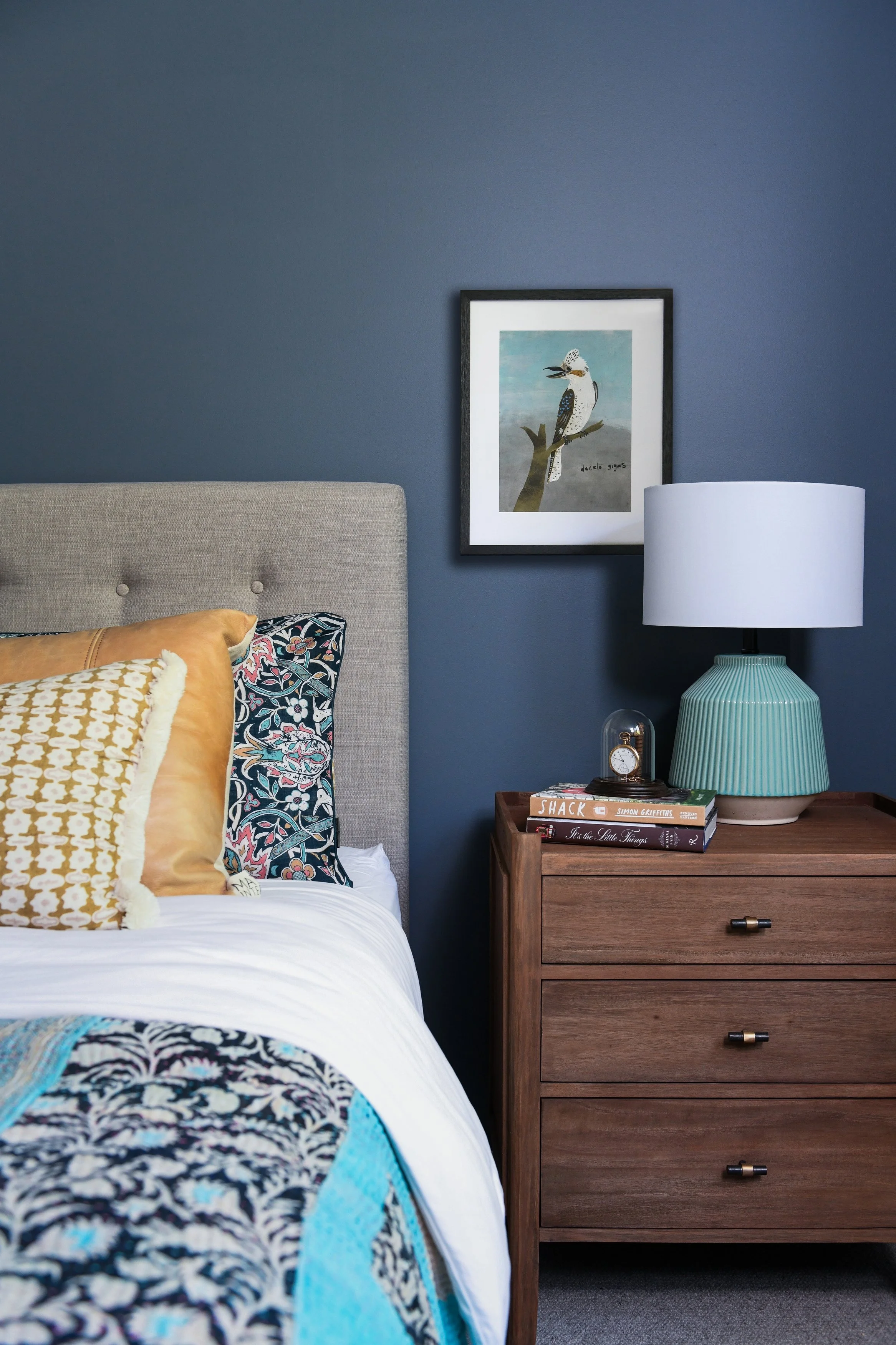 Moody blue bedroom with layered cushions and kookaburra artwork
