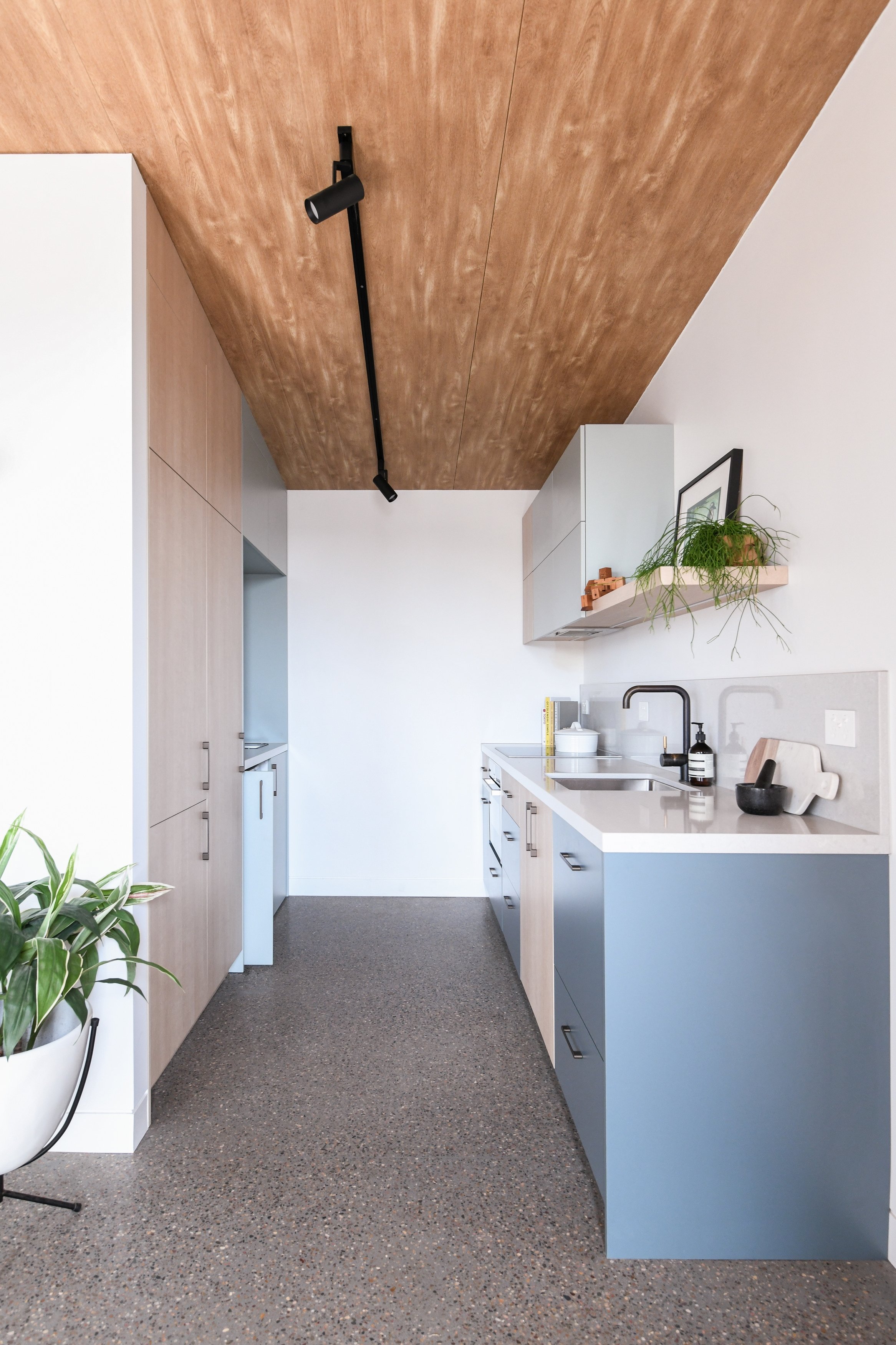 Kitchen and laundry in granny flat studio with poured concrete floor and timber ceiling
