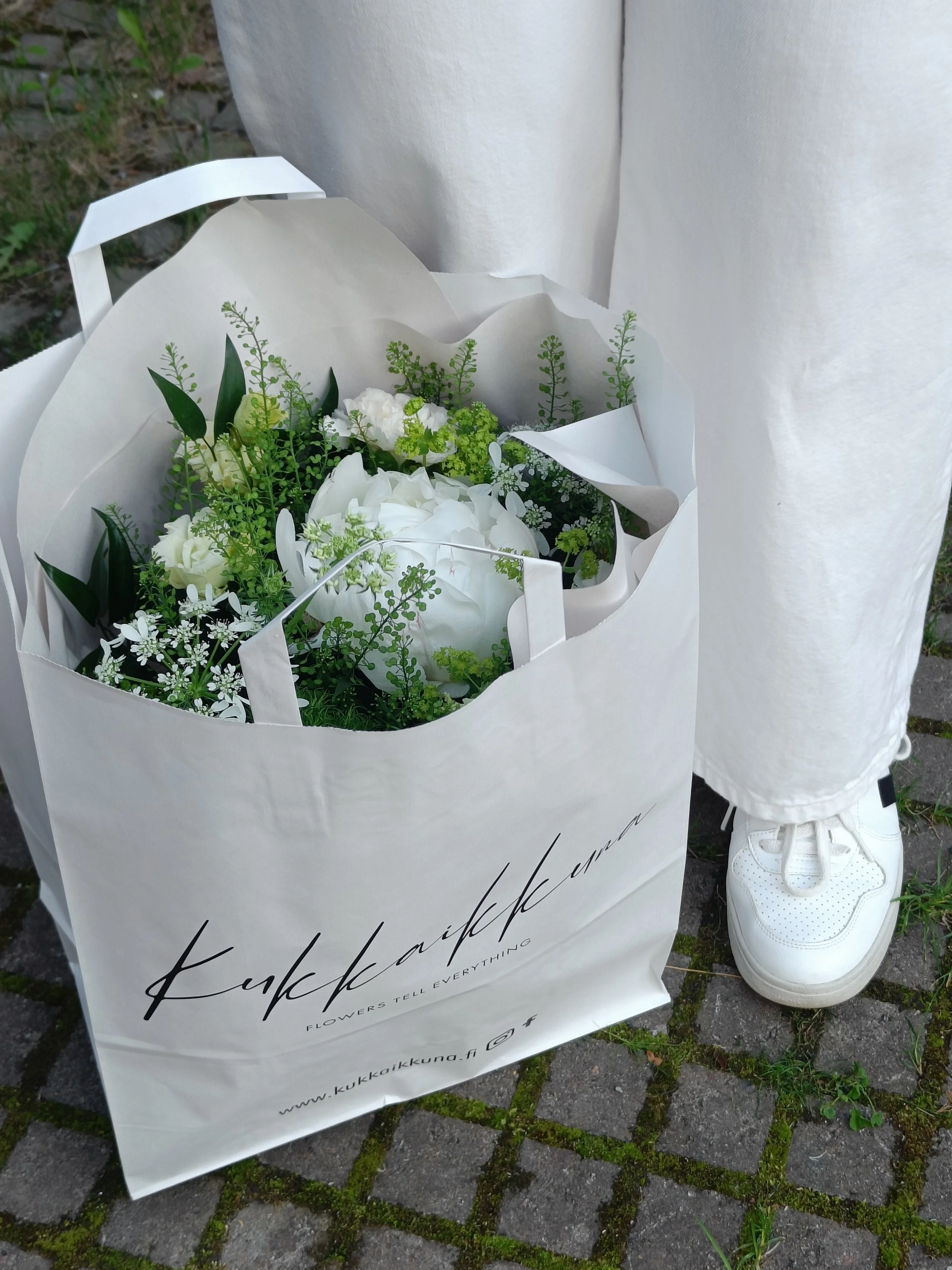 valkoisen ja vihreän värinen kimppu paperikassissa