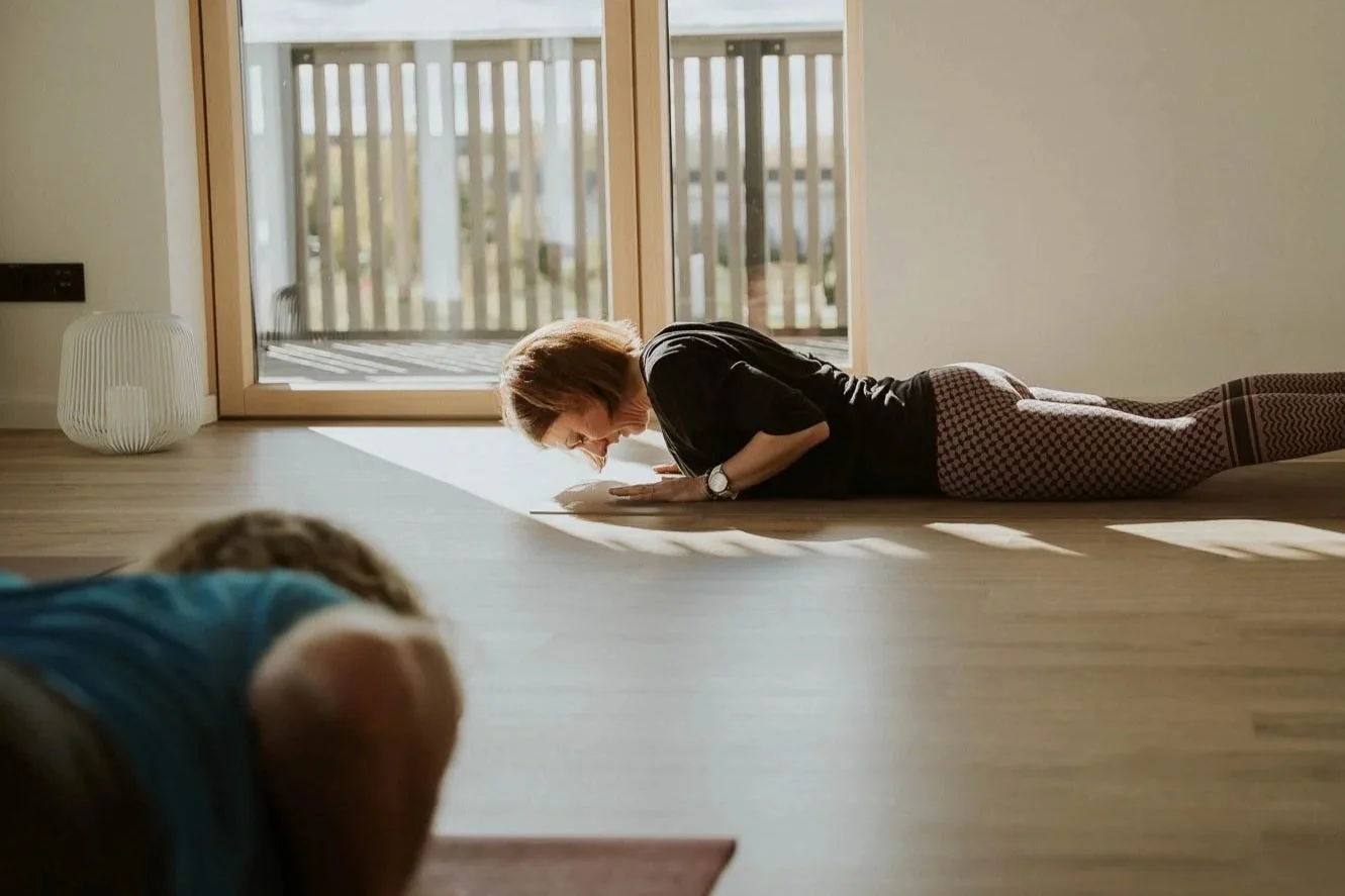 Frau macht einen Yoga- oder Atemübung im Wohnzimmer, liegend auf den Bauch, vor einem großen Fenster