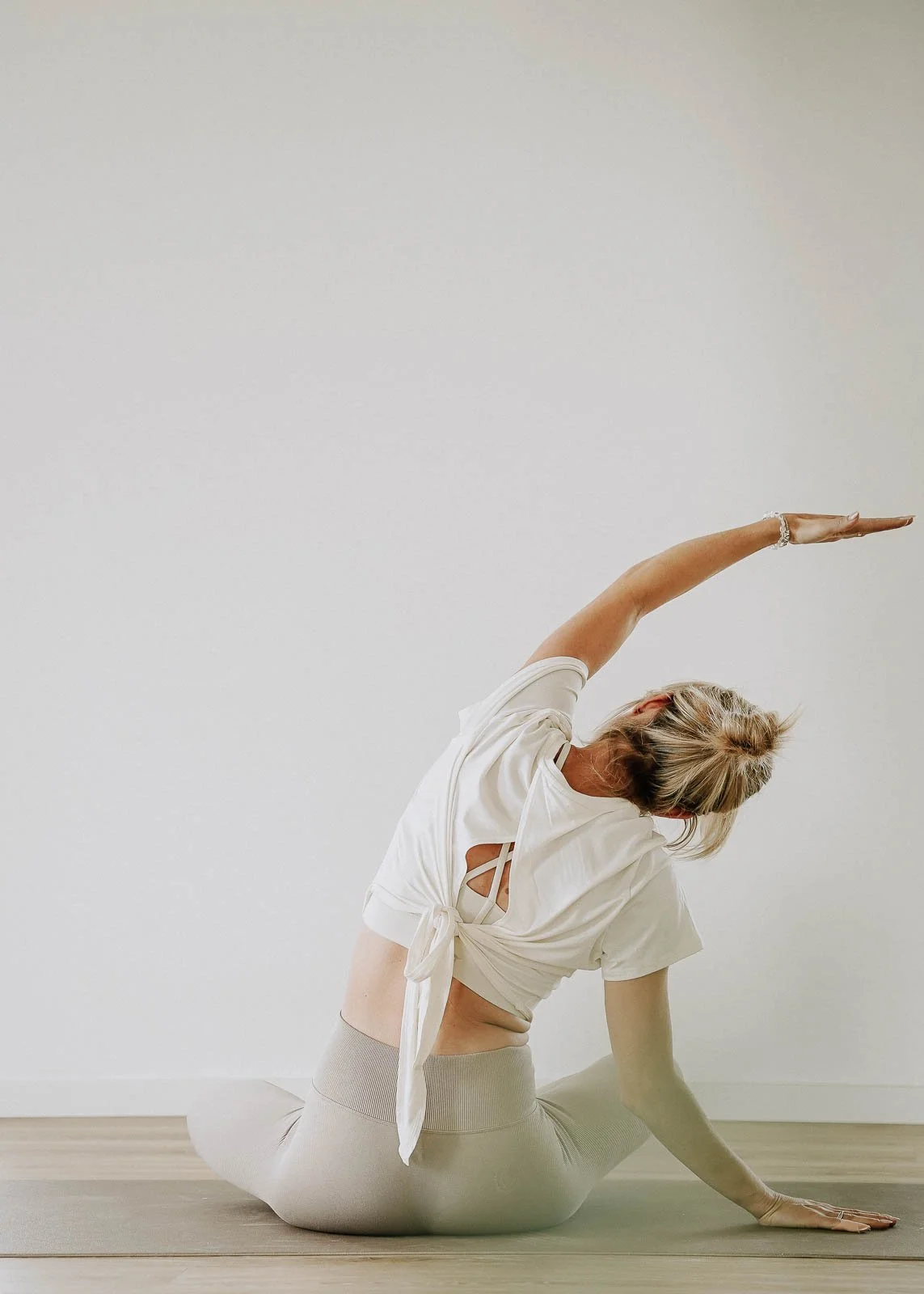 Frau in Yoga-Pose, die auf einer Matte auf dem Boden sitzt, in einer weißen Raumumgebung.