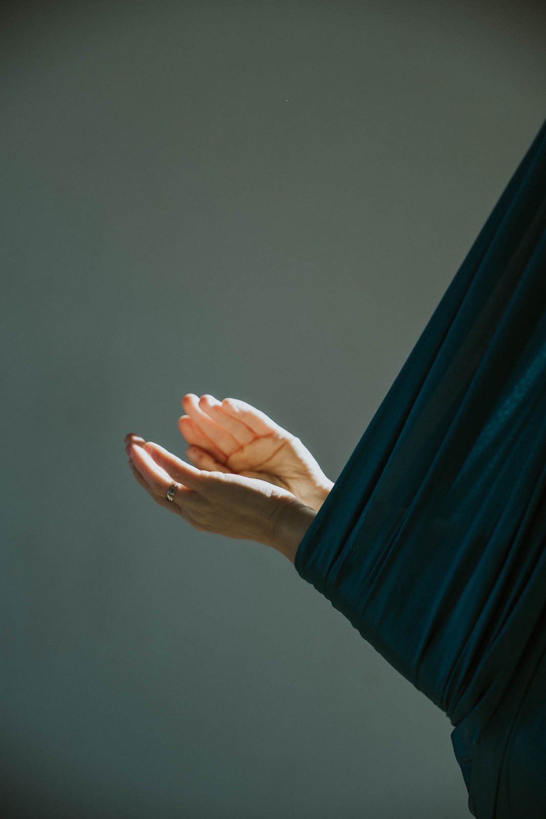 Eine Hand mit einer Goldring trägt einen schwarzen langen Ärmel, die andere Hand wird im Stillen gehalten, wohl beim Meditieren in einem Aerial-Yoga-Tuch.