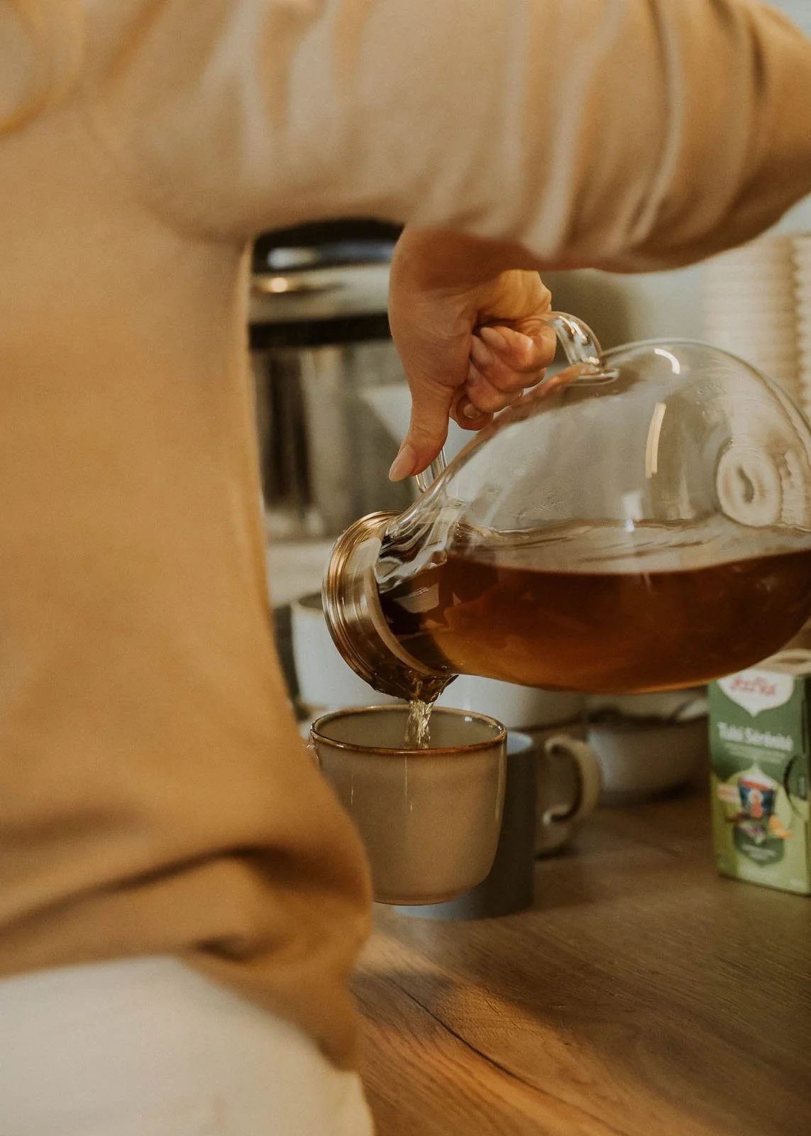 Eine Person gießt Kaffee aus einer Glaskanne in eine Tasse auf einem Holztisch.