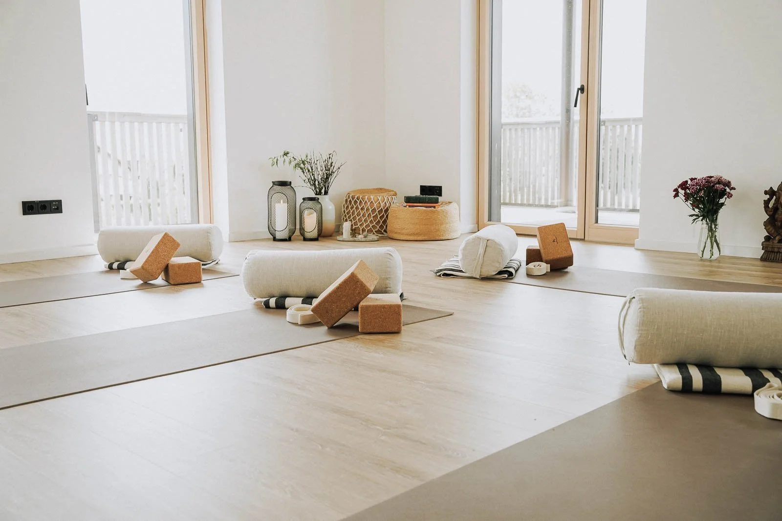 Ein heller Raum mit Yoga-Matten und Yogablöcken, dekoriert mit Blumen, Kerzen und einer Statue, bereit für eine Yoga- oder Meditationssession.