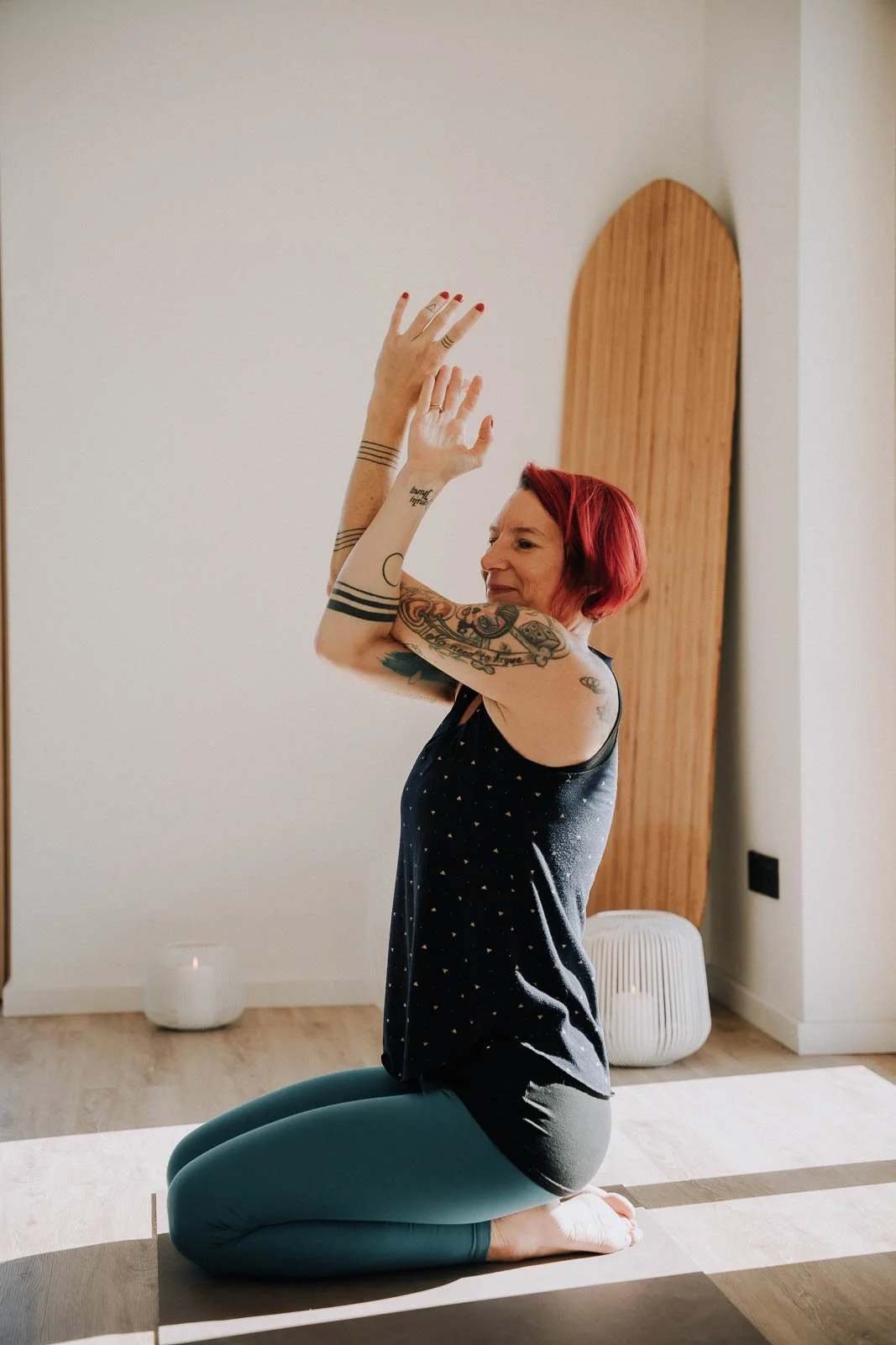 Person auf der Yogamatte im Fersensitz, Arme erhoben, in hellem Raum mit sanftem Licht und dezenten Holzelementen.