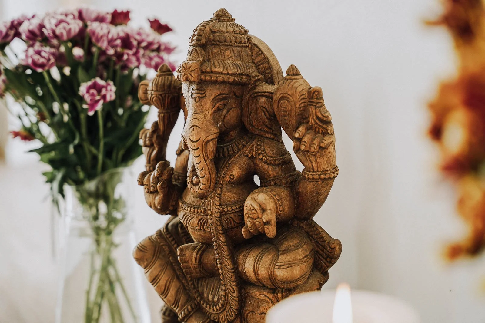 Detailaufnahme einer geschnitzten Holzfigur des hinduistischen Gottes Ganesha, umgeben von Blumen und einer Kerze.