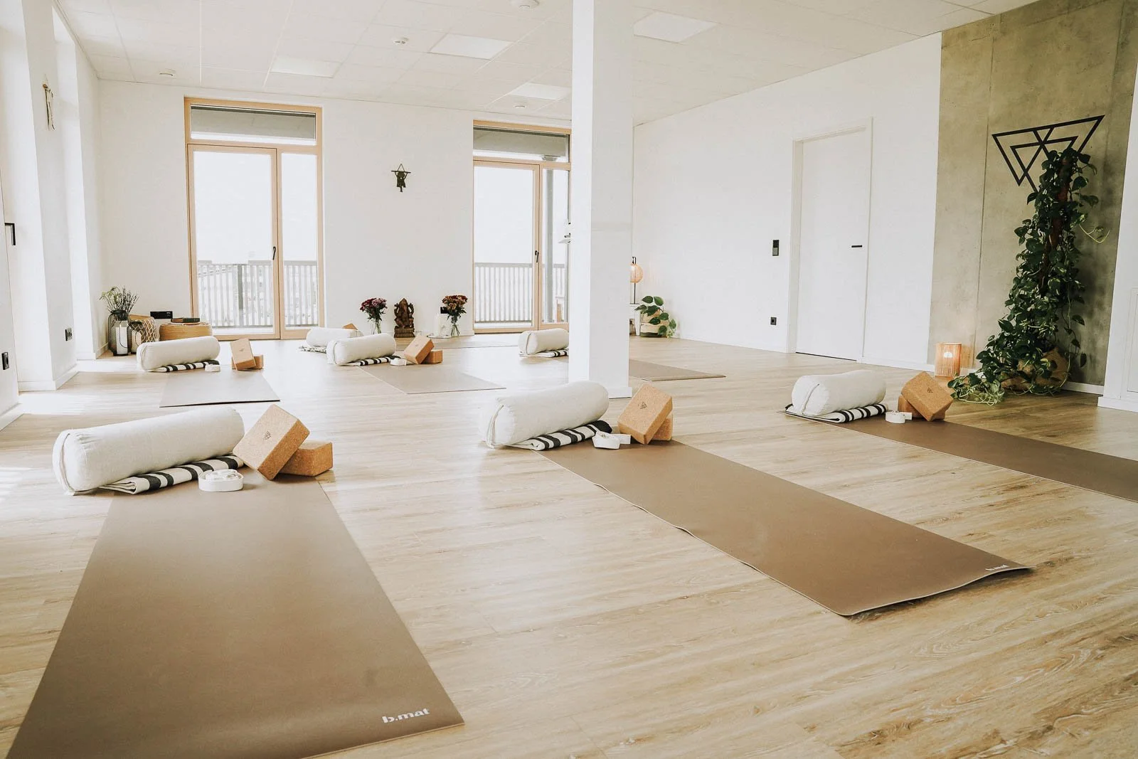 Innenseite eines Yoga-Studios mit Yoga-Matten, Polster und Dekorationen in einem hellen Raum mit großen Fenstern.
