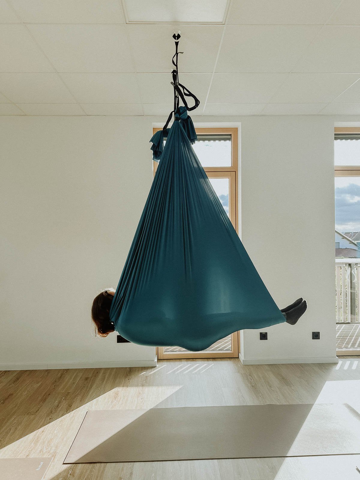 Person in blauer Hängematte im Raum, Sonne scheint durch Fenster.