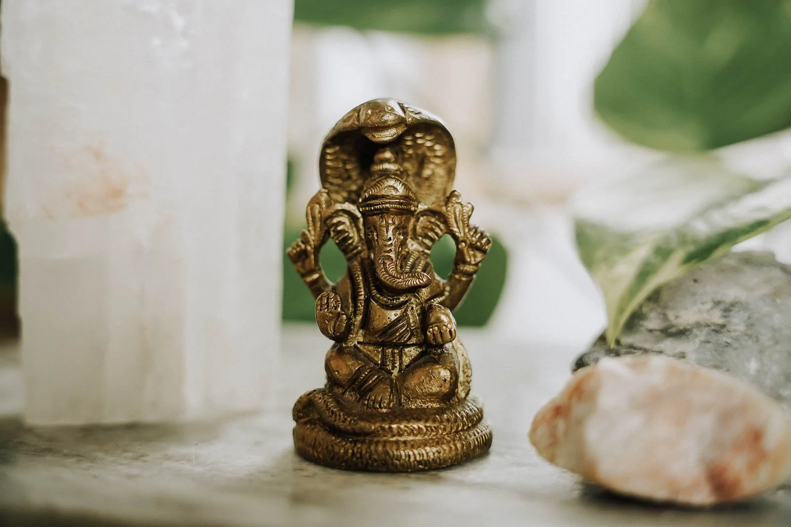 Goldene Ganesha-Figur auf einer Oberfläche, umgeben von Kristallen und Pflanzen.