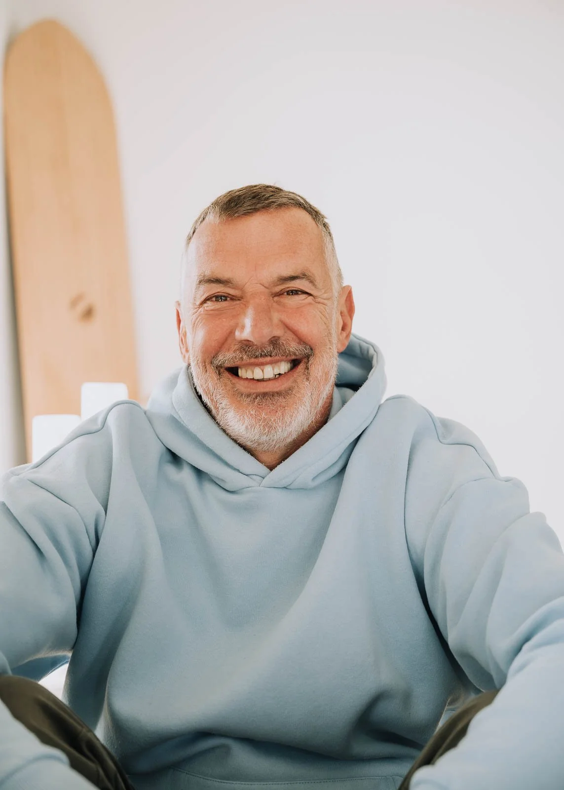 Lächelnde Person in hellblauem Hoodie, frontal sitzend in einem hellen Raum mit ruhigem Hintergrund.