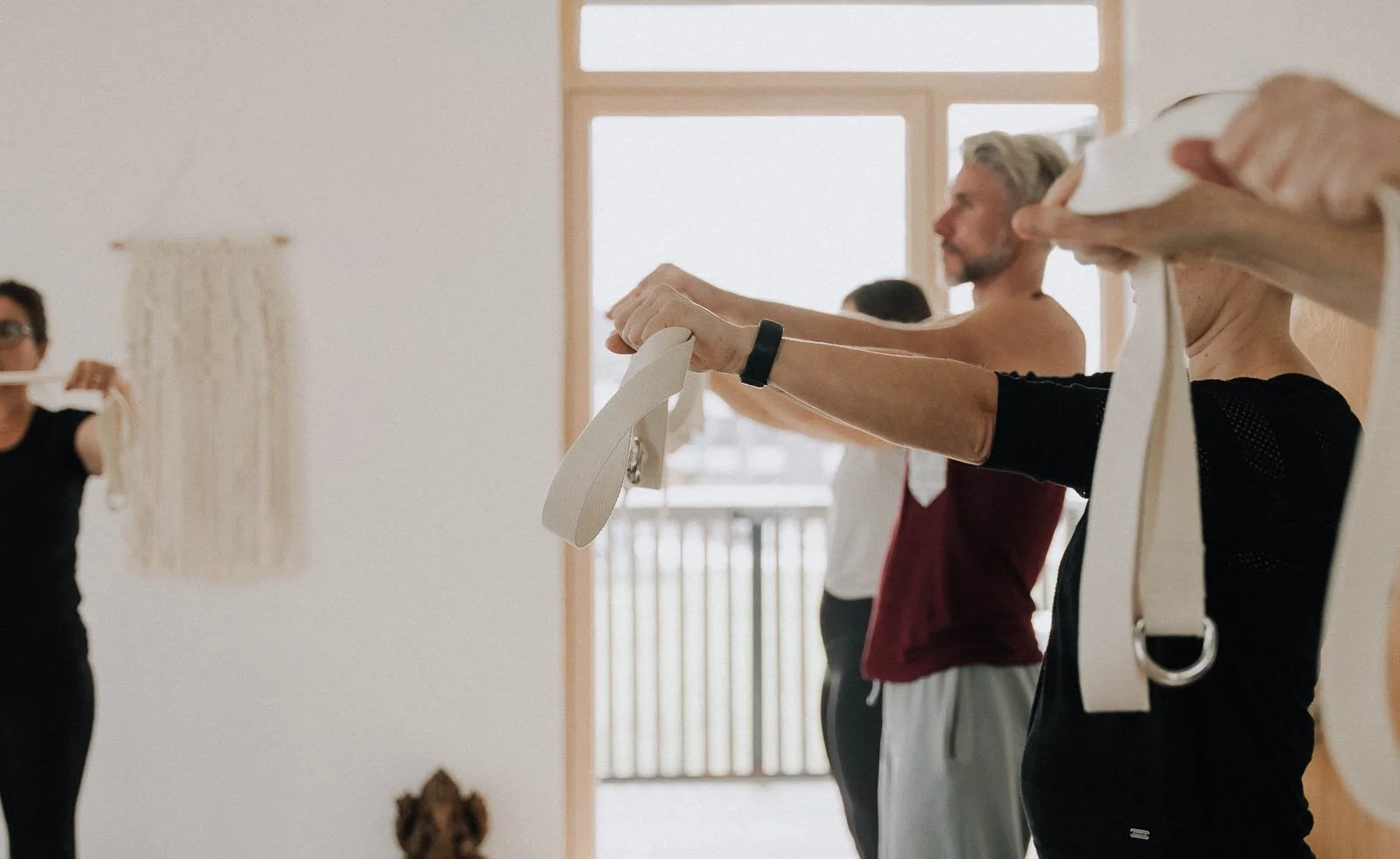 Menschen beim Yoga, die an einer Wand Dehnübungen machen, in einem Raum mit großer Fensterfront