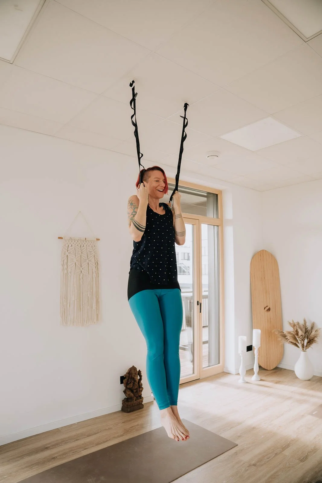 Frau macht Yoga an einem Seil an der Decke in einem hellen Zimmer.