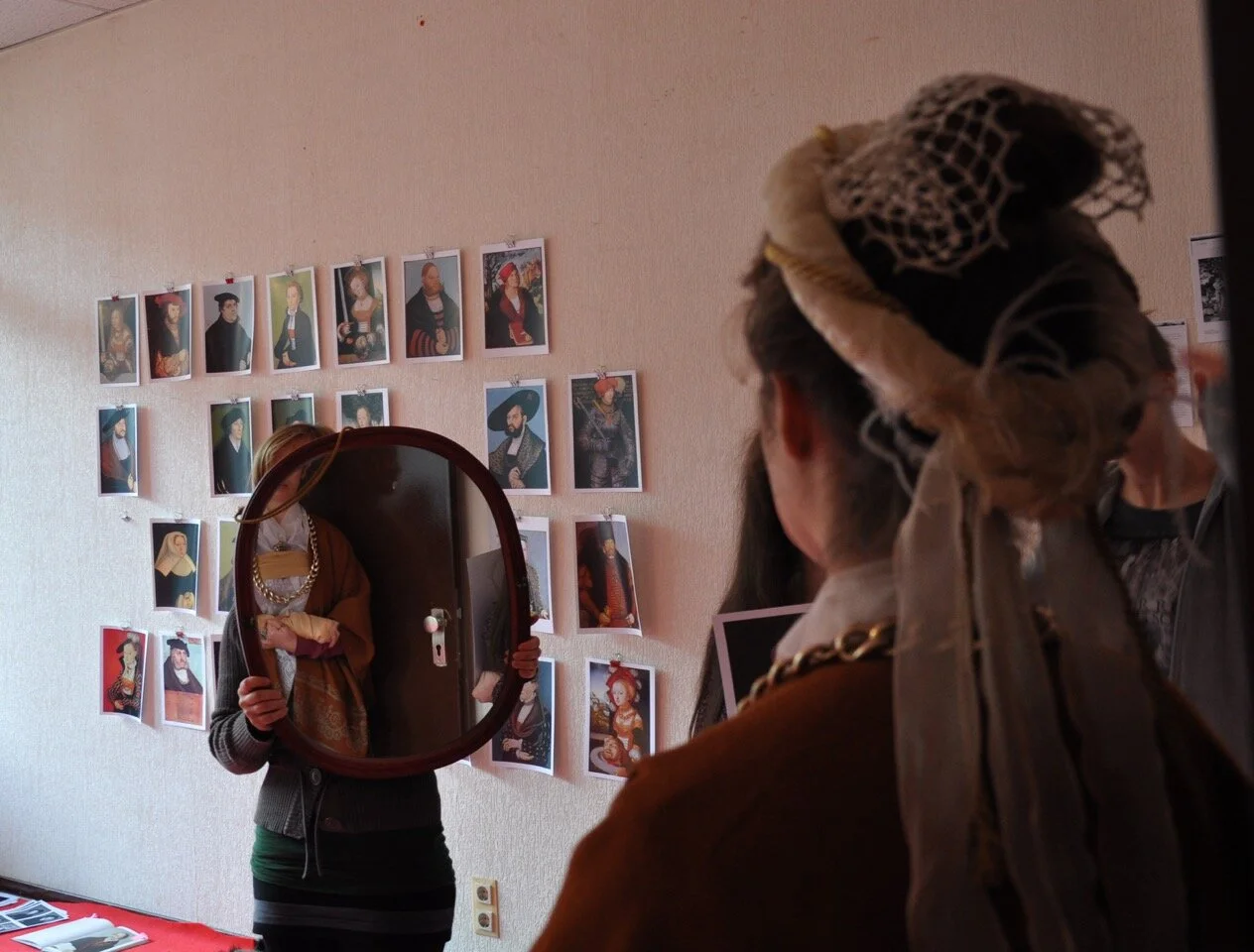 Menschen stehen im Raum des „Alice-Museum für Kinder“ im FEZ-Berlin. Bilder des Künstlers Lucas Cranach hängen an der Wand und eine Frau hält ein Spiegel.