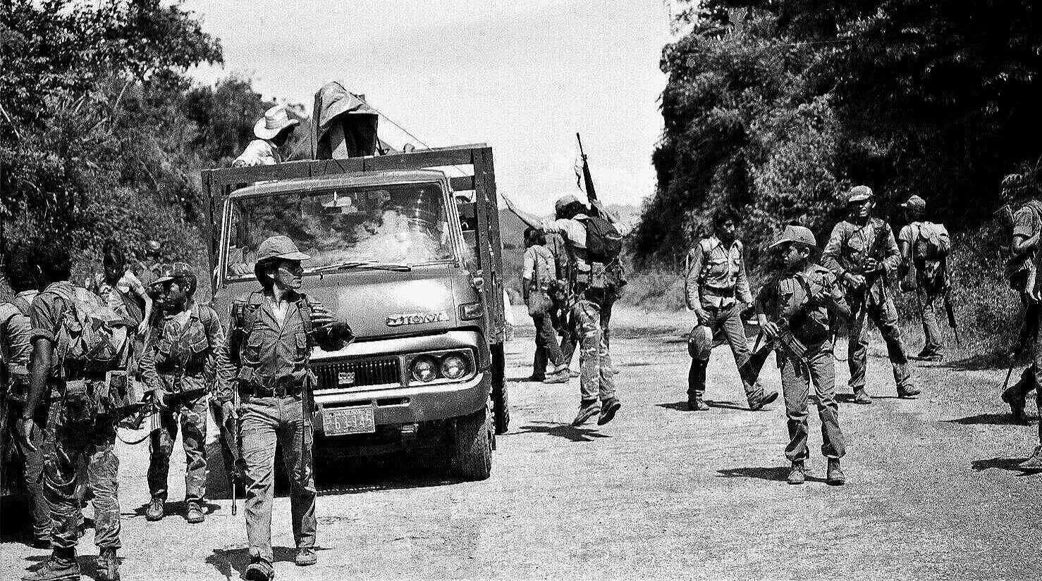 MIDAIR DISMOUNT  —  young guerrillas unloading from back of truck, road to La Palma