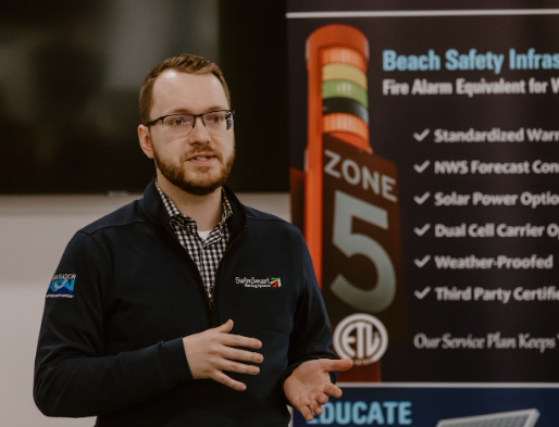 Man with beard and glasses presenting in front of banner