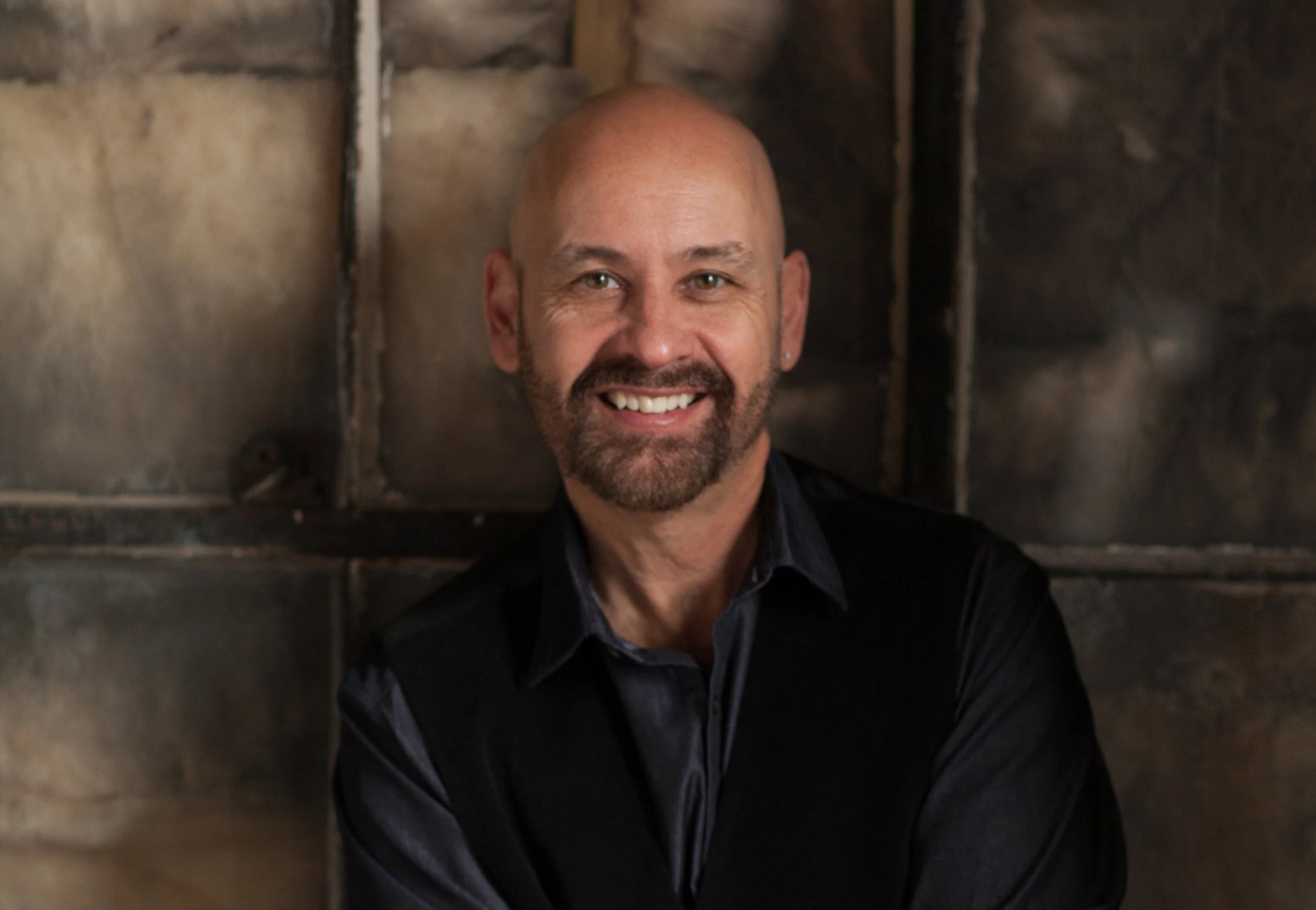 Smiling man with beard in black vest and grey shirt