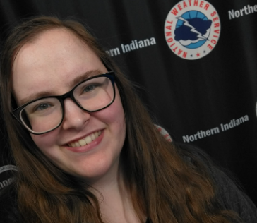 Smiling woman with long hair and glasses against national weather service backdrop