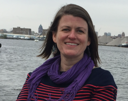 Smiling woman with dark hair and purple scarf with water in the background