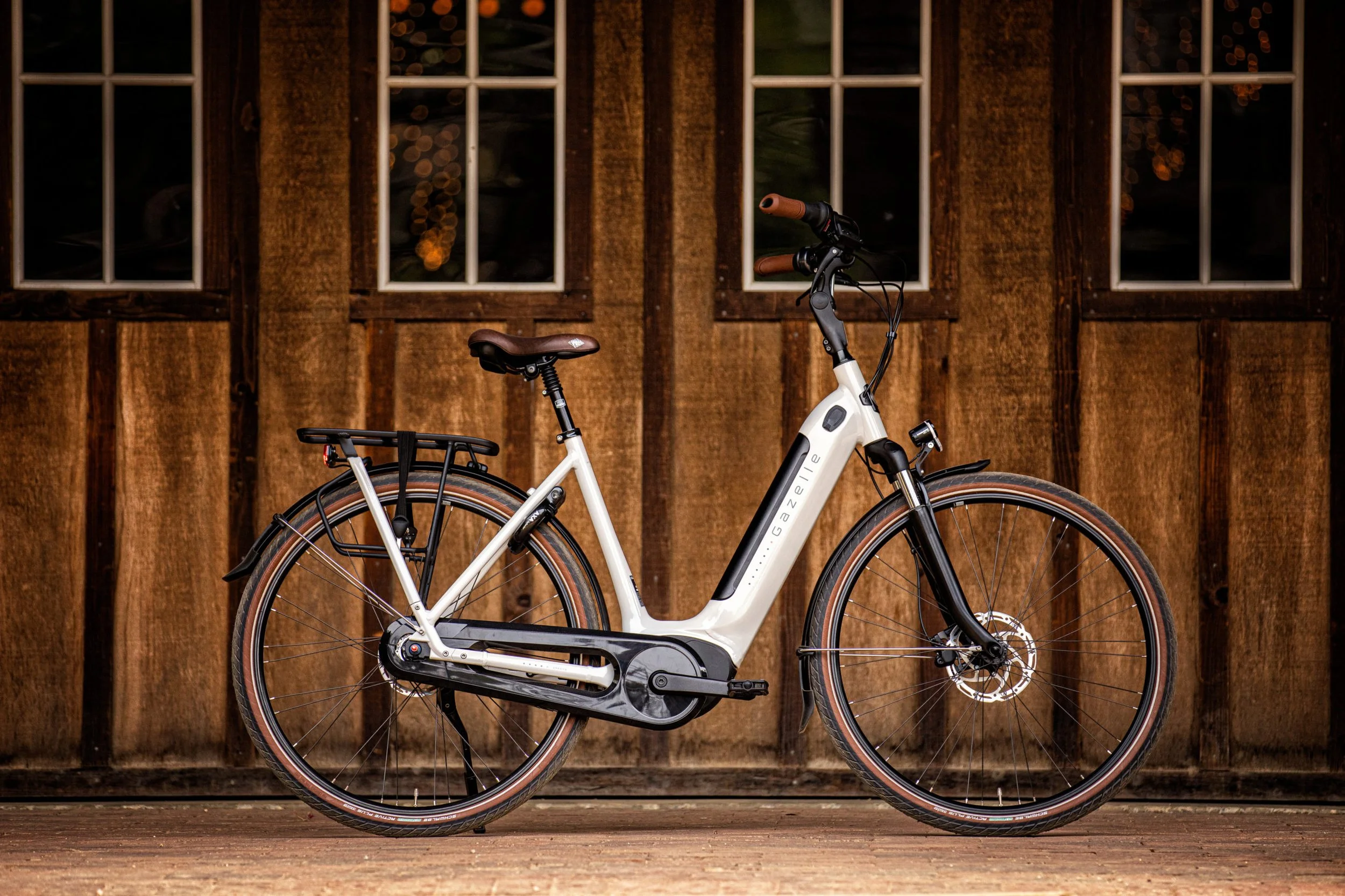 An electric bicycle parked in front of a wooden building with eight windows, illuminated lights visible inside.