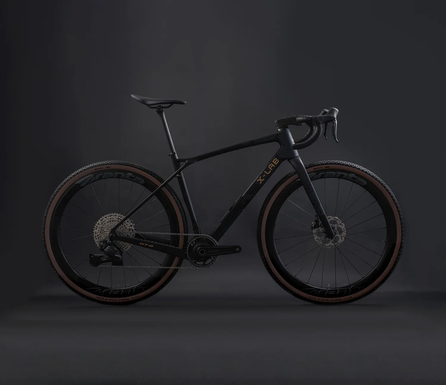A sleek black carbon fiber road bicycle with tan colored tires and disc brakes, set against a dark background.