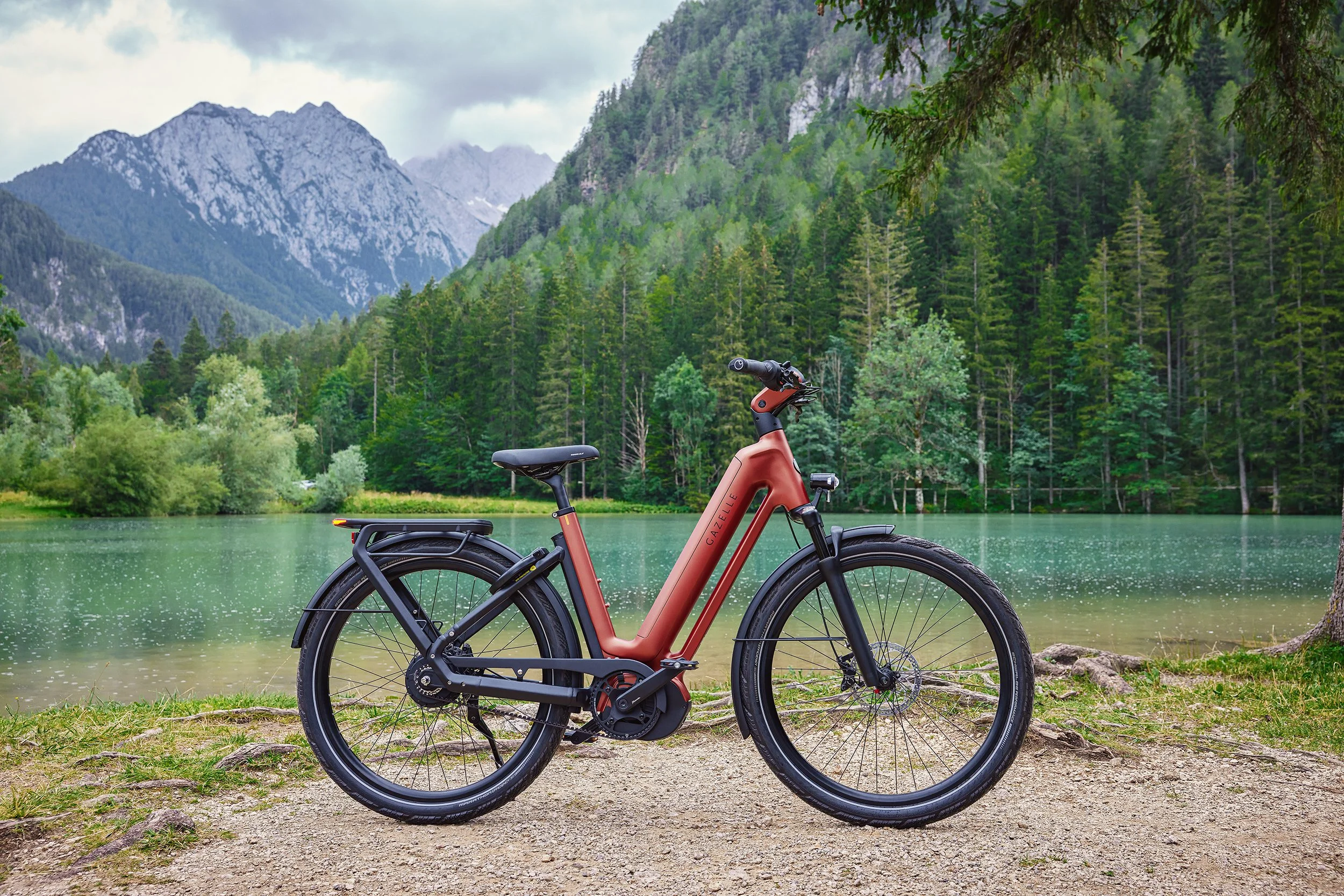 Electric bicycle parked on a dirt path by a lake with forested mountains in the background.