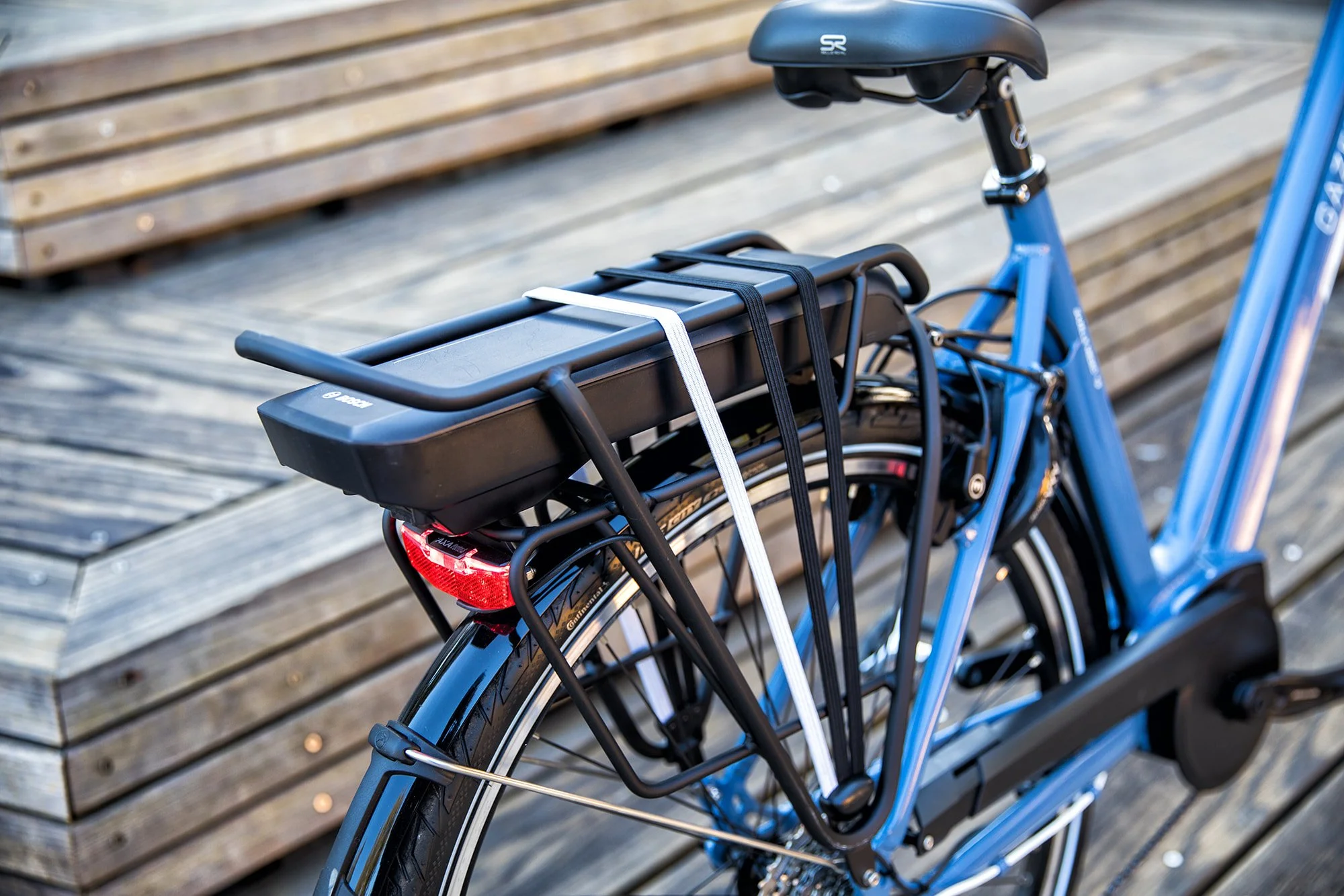 Blue bicycle with a saddle, rear rack, and rear light parked next to a wooden bench.