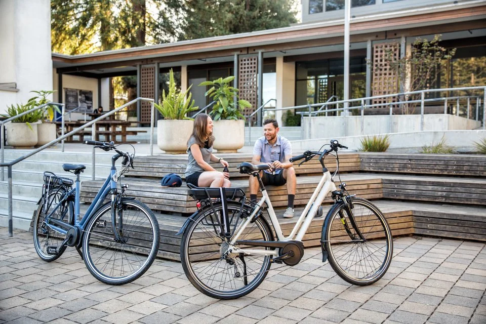 Two people sitting and talking on steps in front of a building, with two bikes parked nearby.