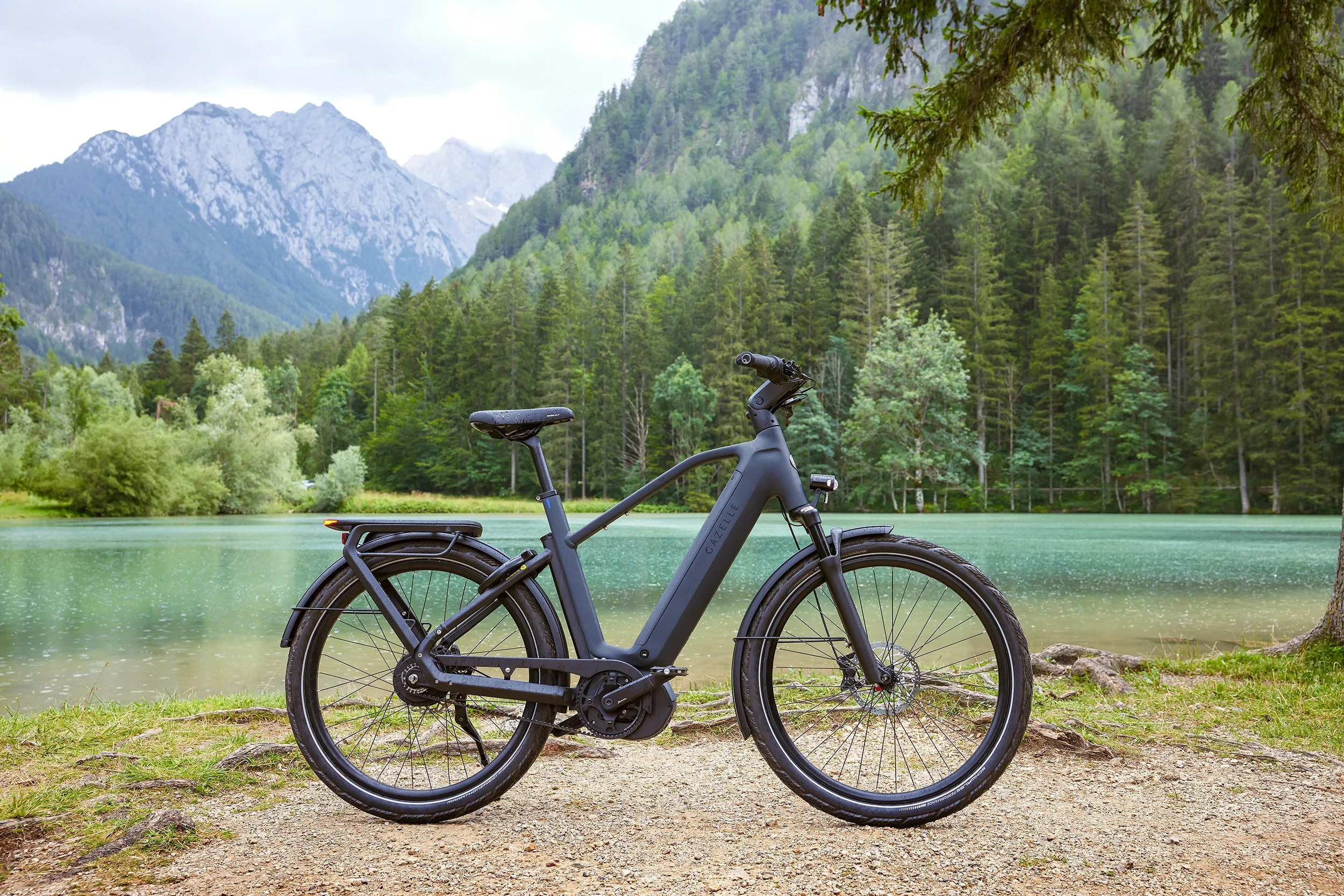 Electric mountain bike parked on a dirt path beside a lake with a forest and mountains in the background.