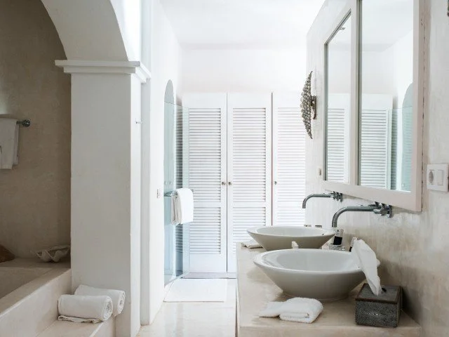Bathroom with dual vessel sinks, large mirror, white towel, white folding screen, and a shower area.