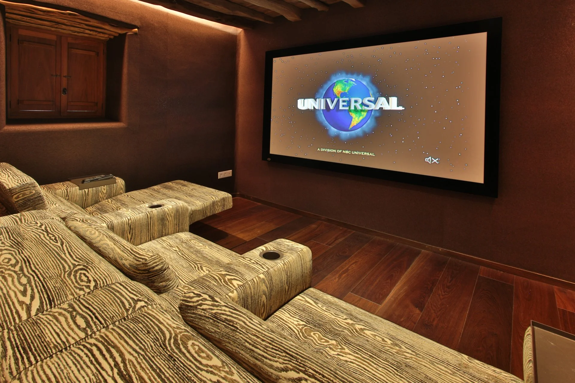 Home theater room with patterned recliner sofa facing a large flat-screen TV displaying the Universal Pictures logo.