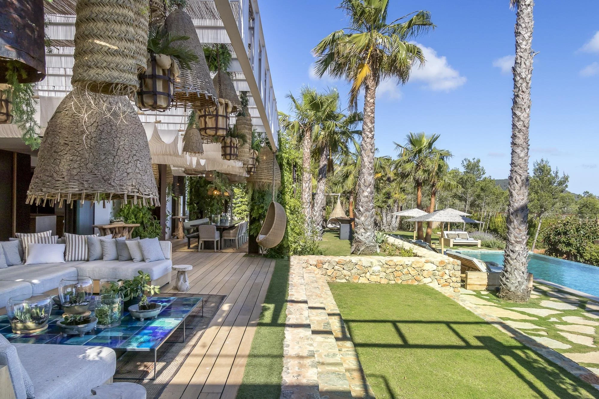 Outdoor patio area with seating, table, and pool surrounded by tall palm trees on a bright, sunny day.