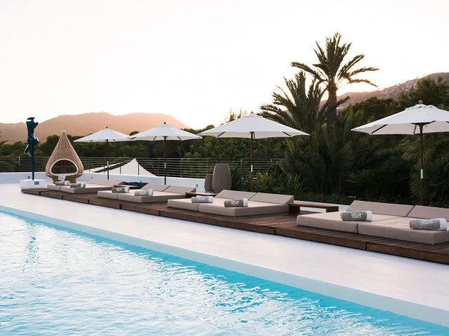 Poolside lounge area with sunbeds, umbrellas, and palm trees at sunset.