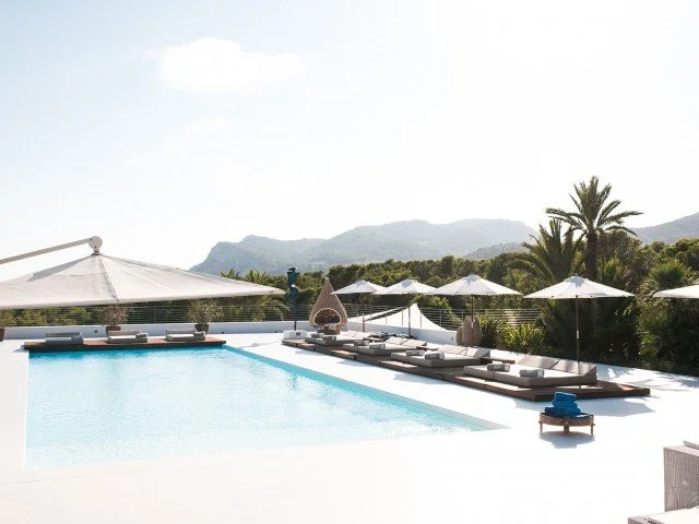 Luxury rooftop pool area with lounge chairs, umbrellas, and scenic mountain view in the background.