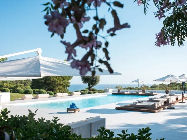 Poolside lounge chairs and umbrellas at a resort with a view of the ocean