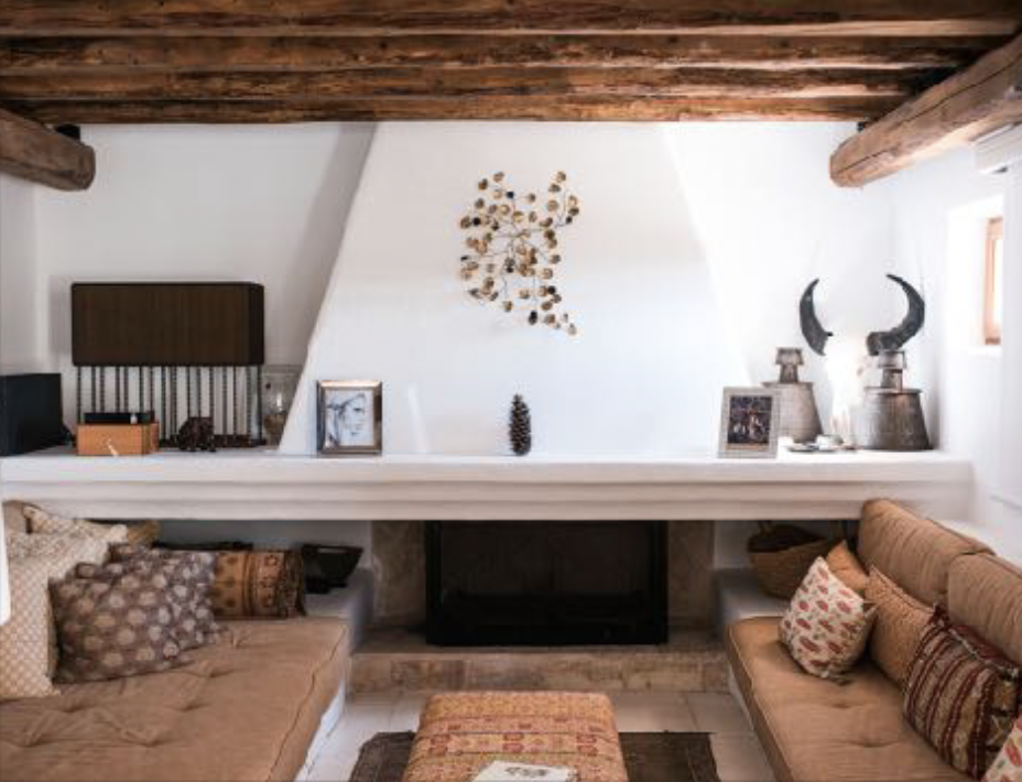 Living room with sloped ceiling, wooden beams, a white fireplace, and two tan sofas with patterned pillows.