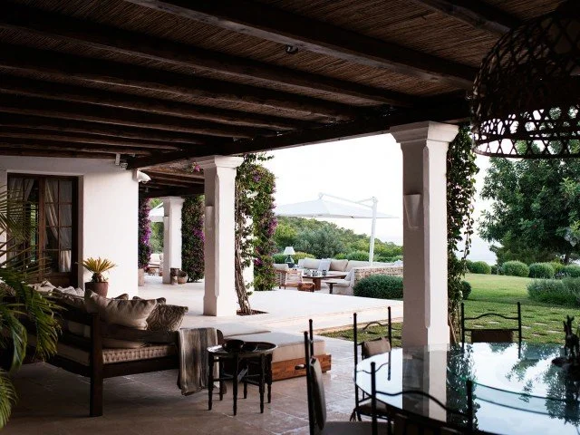 Outdoor patio with seating area, plants, and view of green landscape and distant mountains.