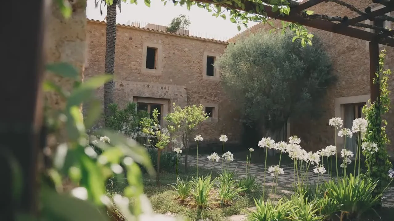 A courtyard with a stone building, lush greenery, and blooming white flowers.