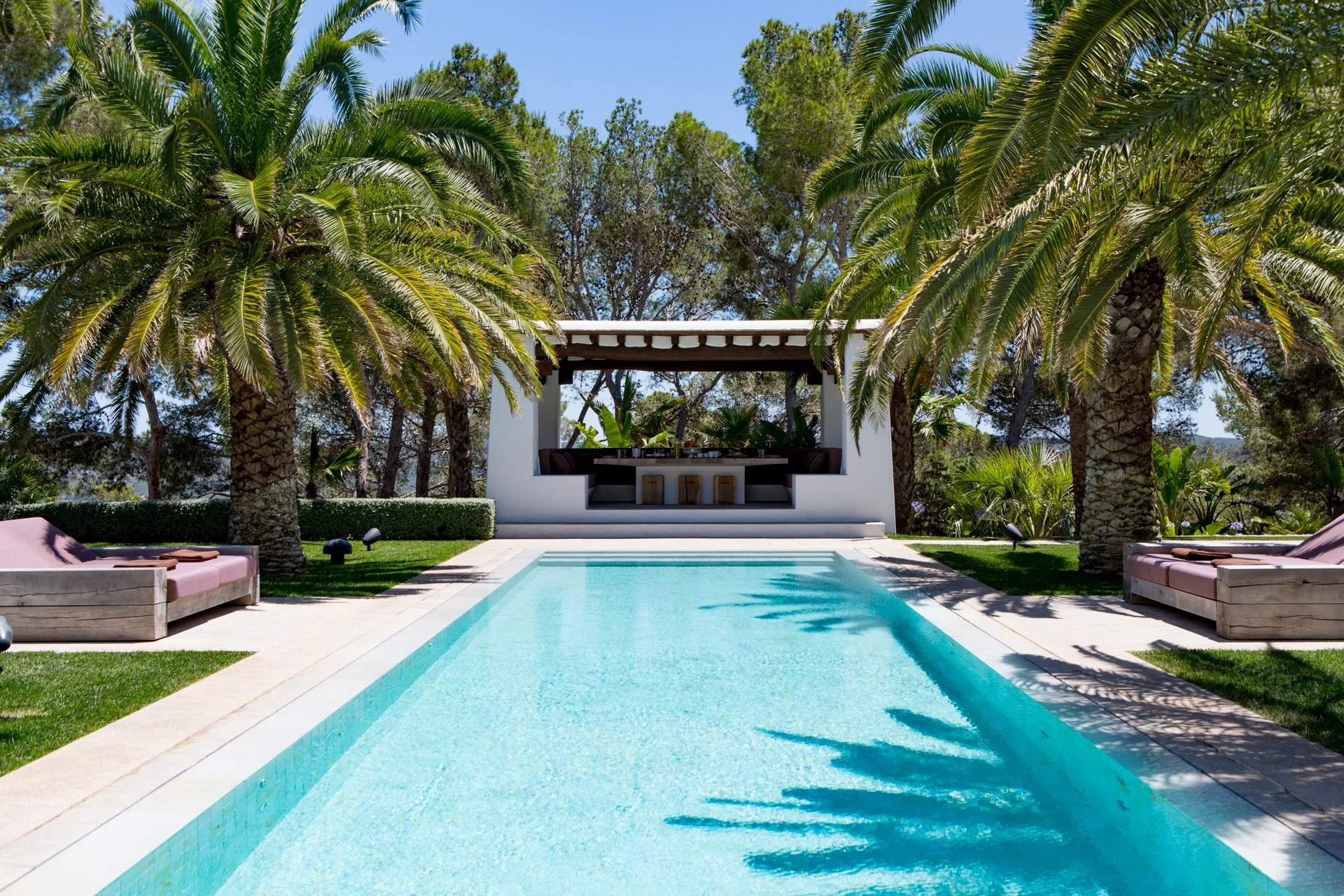 Luxury backyard with a swimming pool, surrounded by palm trees, outdoor seating, and a shaded lounge area.