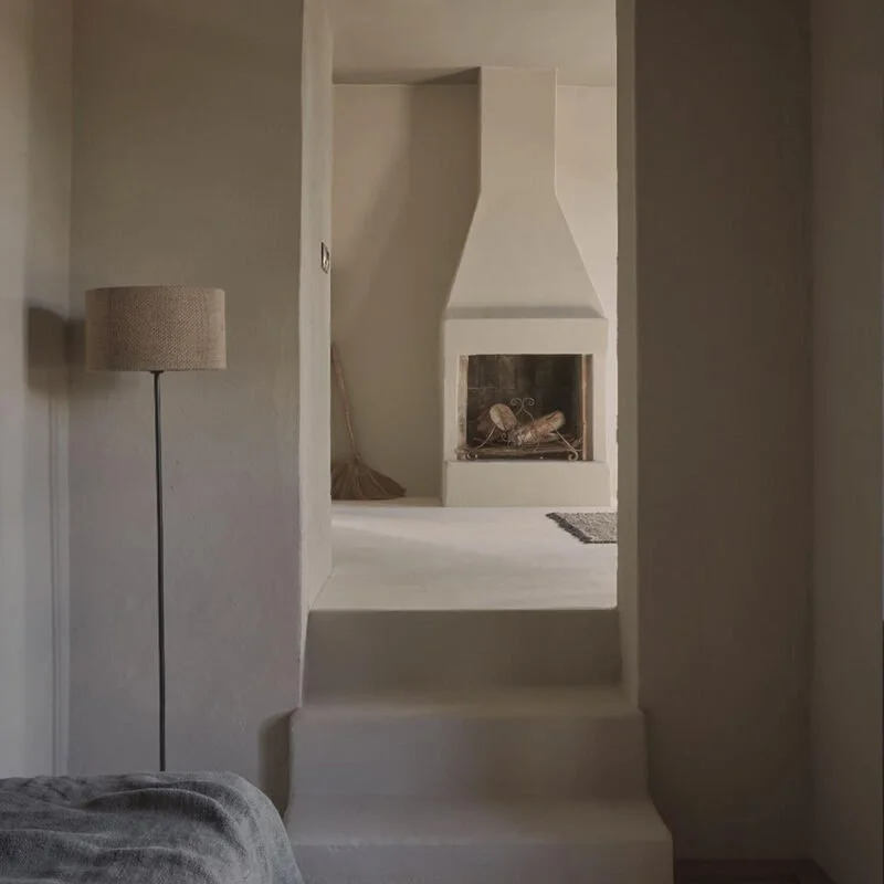 A cozy living room with a beige fireplace, a floor lamp with a beige shade, and a gray couch in the foreground.