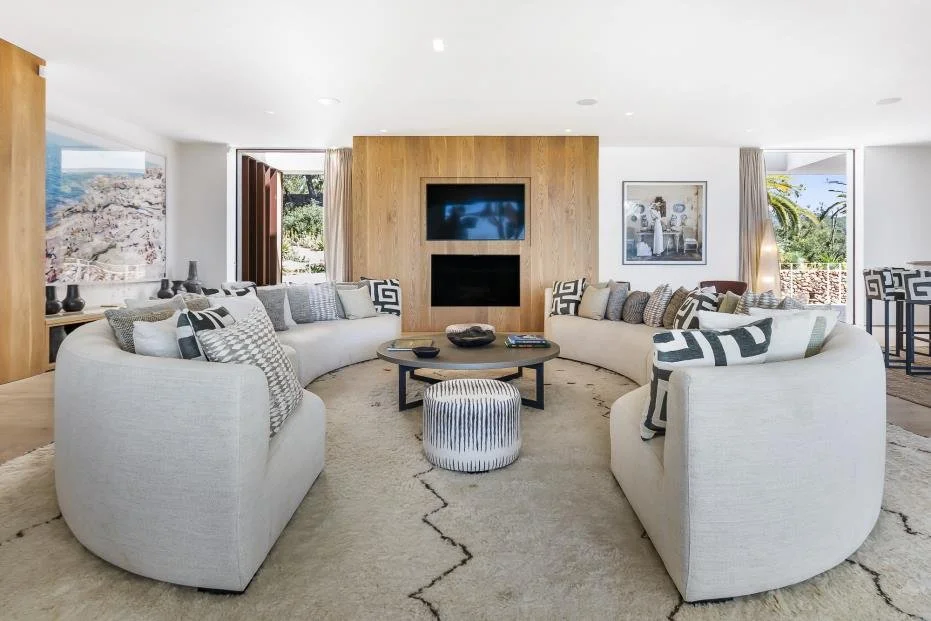 Living room with white curved sofas, a round coffee table, and a wall-mounted television against wooden paneling.