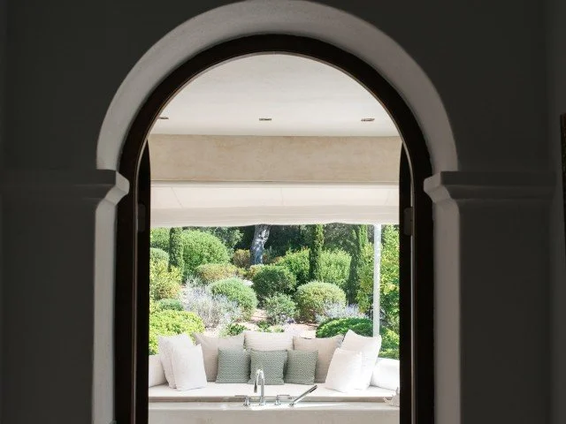 View of a lush garden through an arched doorway with a white outdoor sofa and cushions.