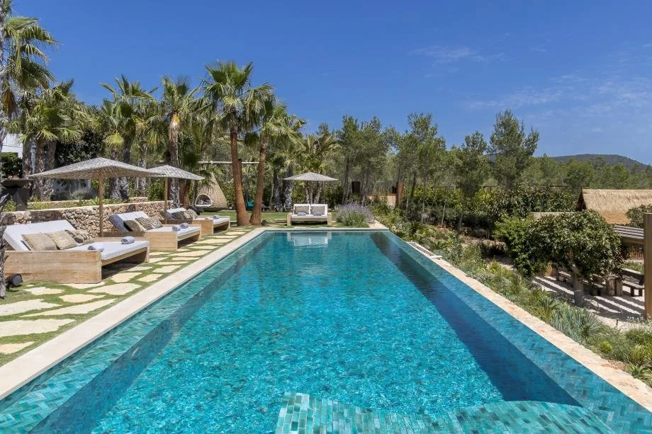Luxury outdoor swimming pool with lounge chairs, umbrellas, and palm trees in a tropical setting.