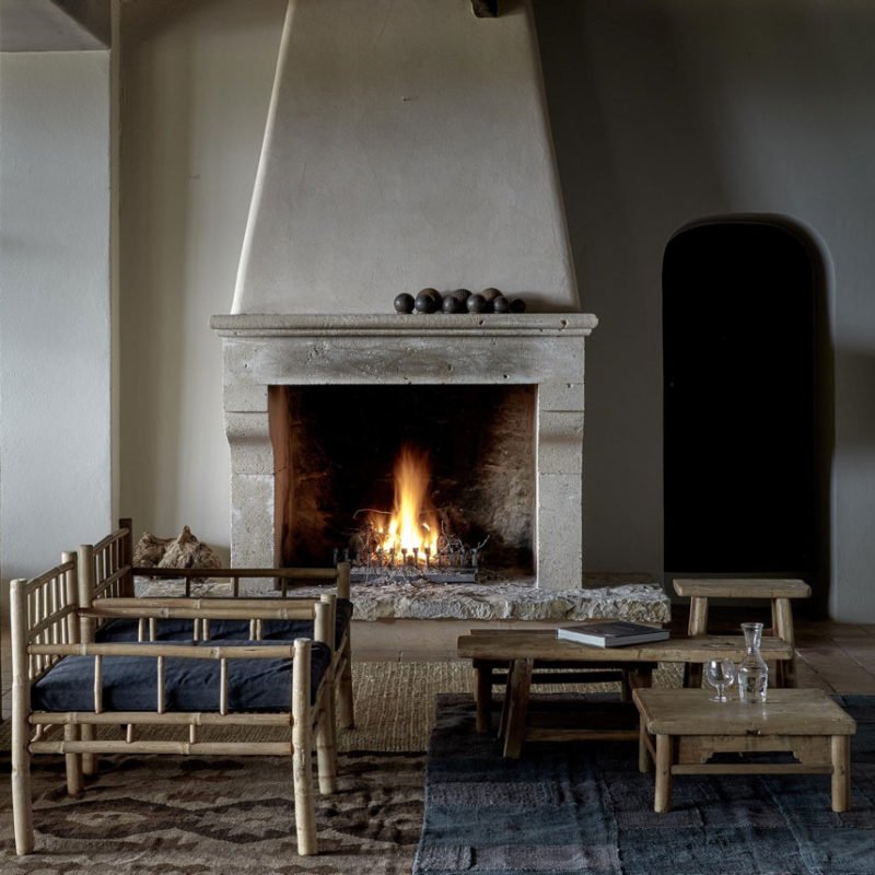 Living room with a lit fireplace, wooden furniture, and decorative objects on a coffee table, with a neutral color palette.