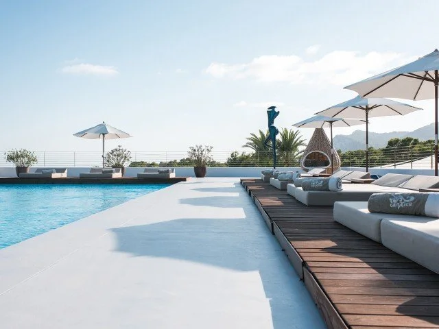 Luxury rooftop pool area with lounge chairs, umbrellas, and a view of distant mountains.