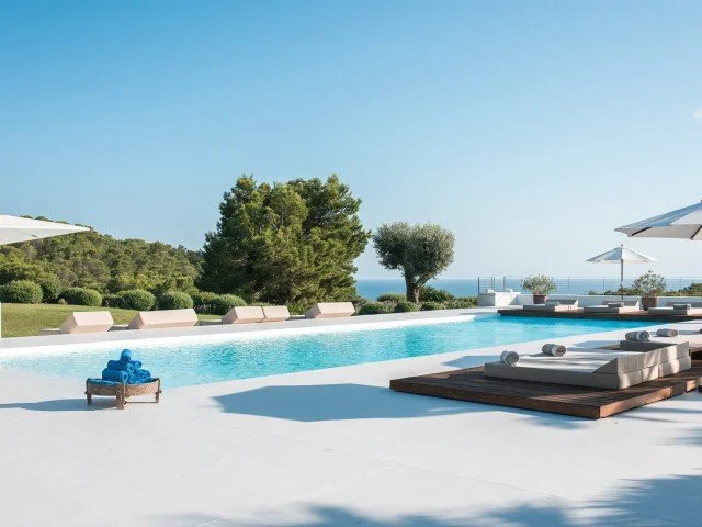 Luxury poolside area with lounge chairs, umbrellas, and scenic greenery overlooking the ocean.