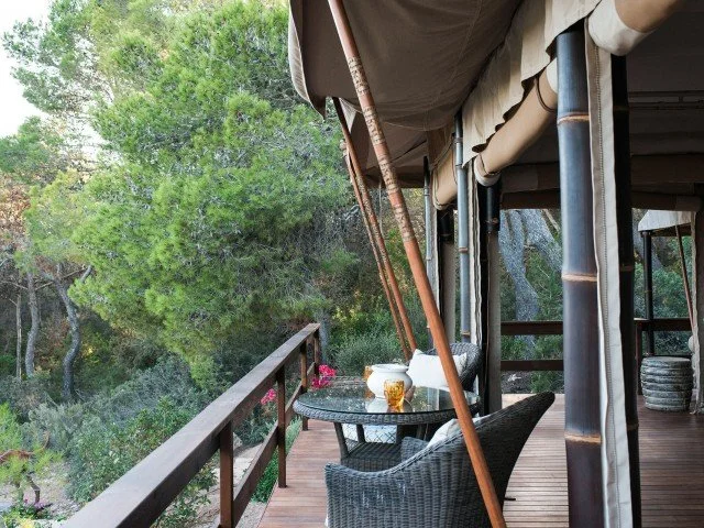 A balcony with wicker chairs, a table with a tea pot and cups, surrounded by lush greenery.