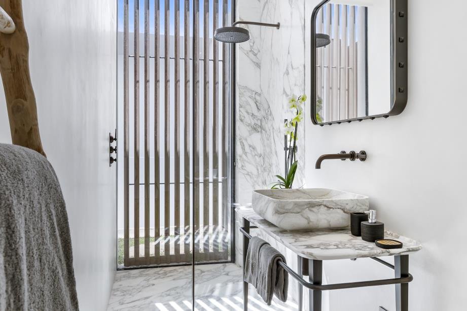 Modern bathroom with marble sink, black faucet, and mirror, with a wood slat door and a plant.