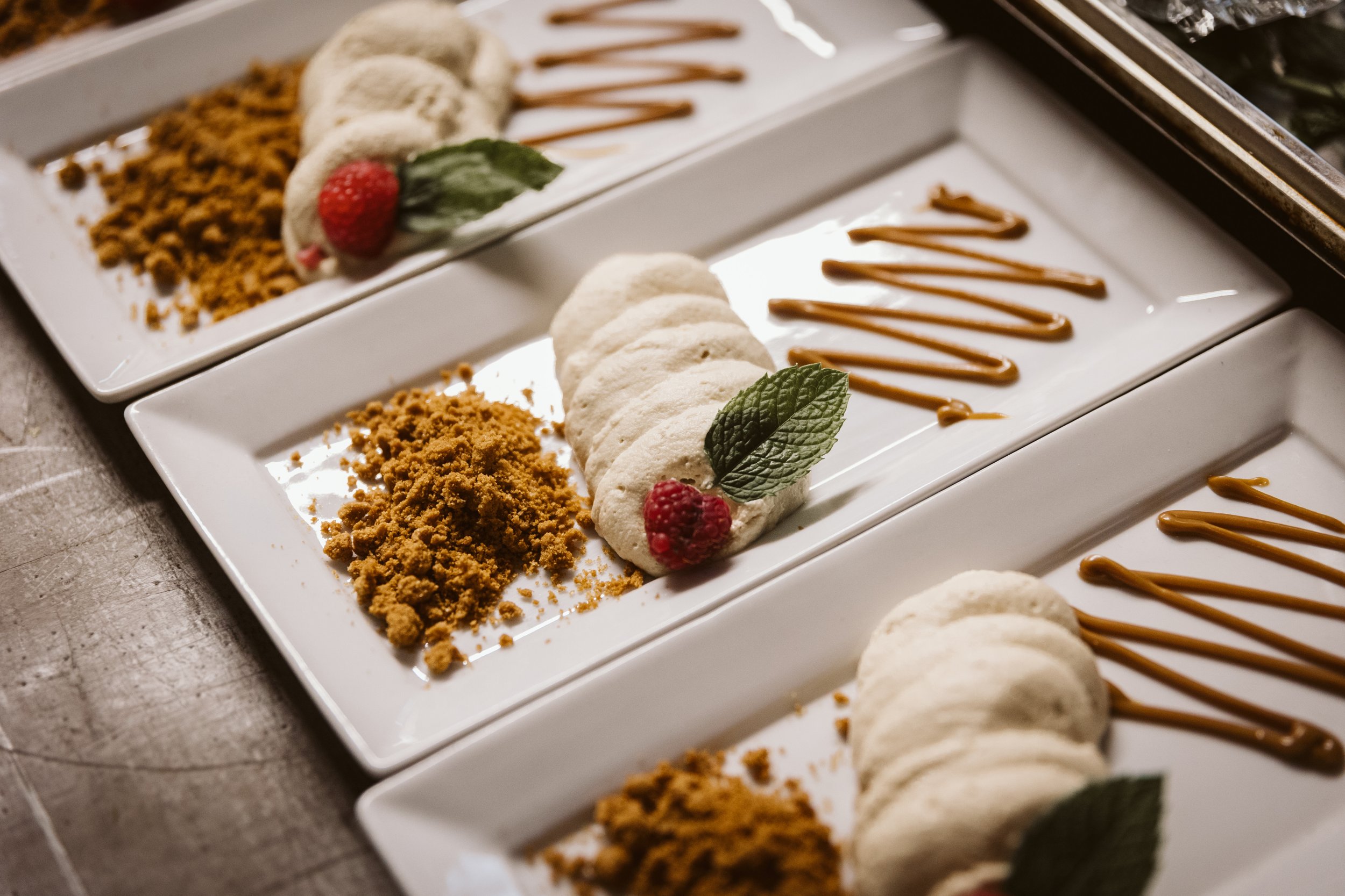 Dessert plates with sliced bananas, crumbly topping, a raspberry, a mint leaf, and caramel drizzle