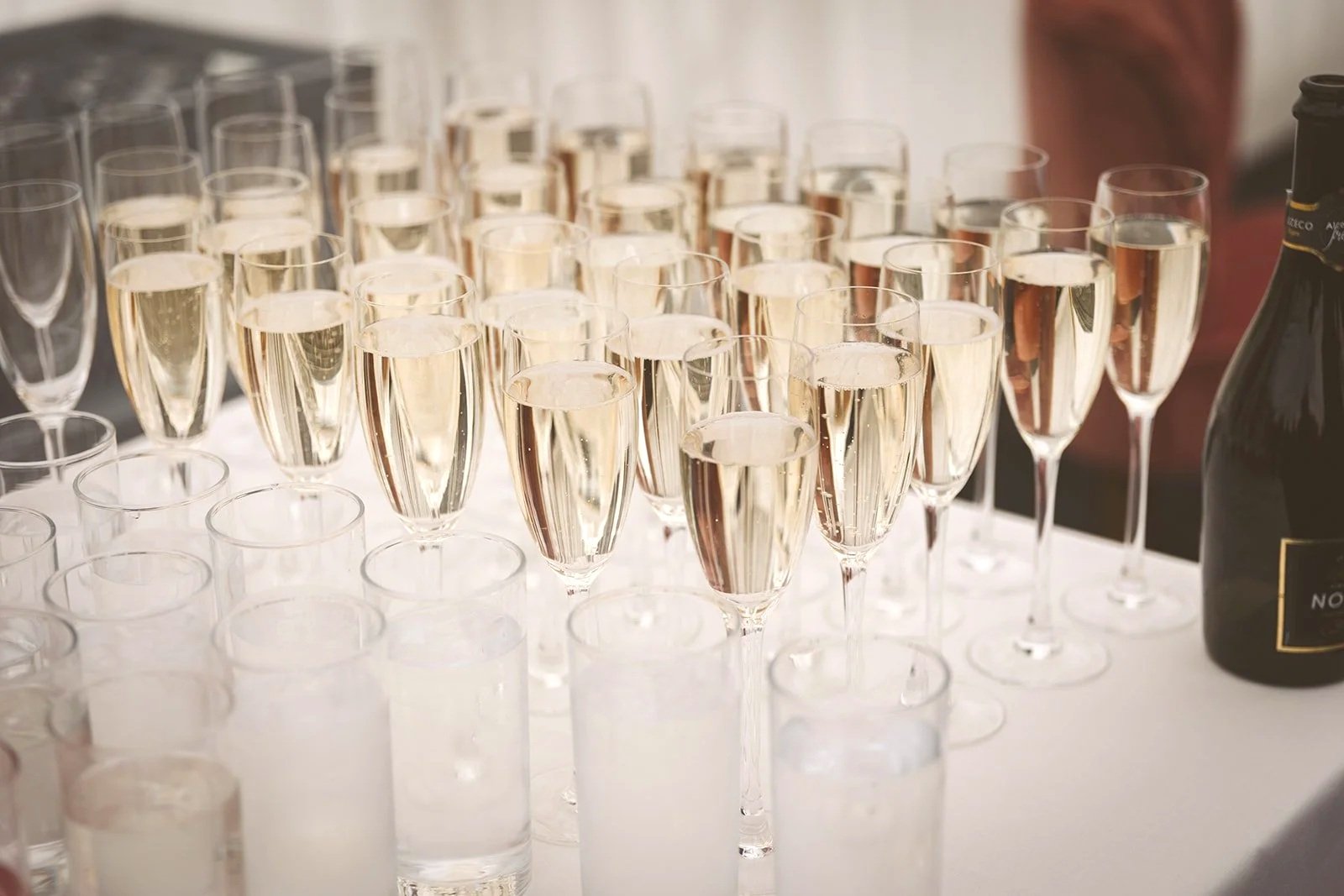 Multiple glasses of champagne and empty shot glasses on a table, with a champagne bottle nearby.